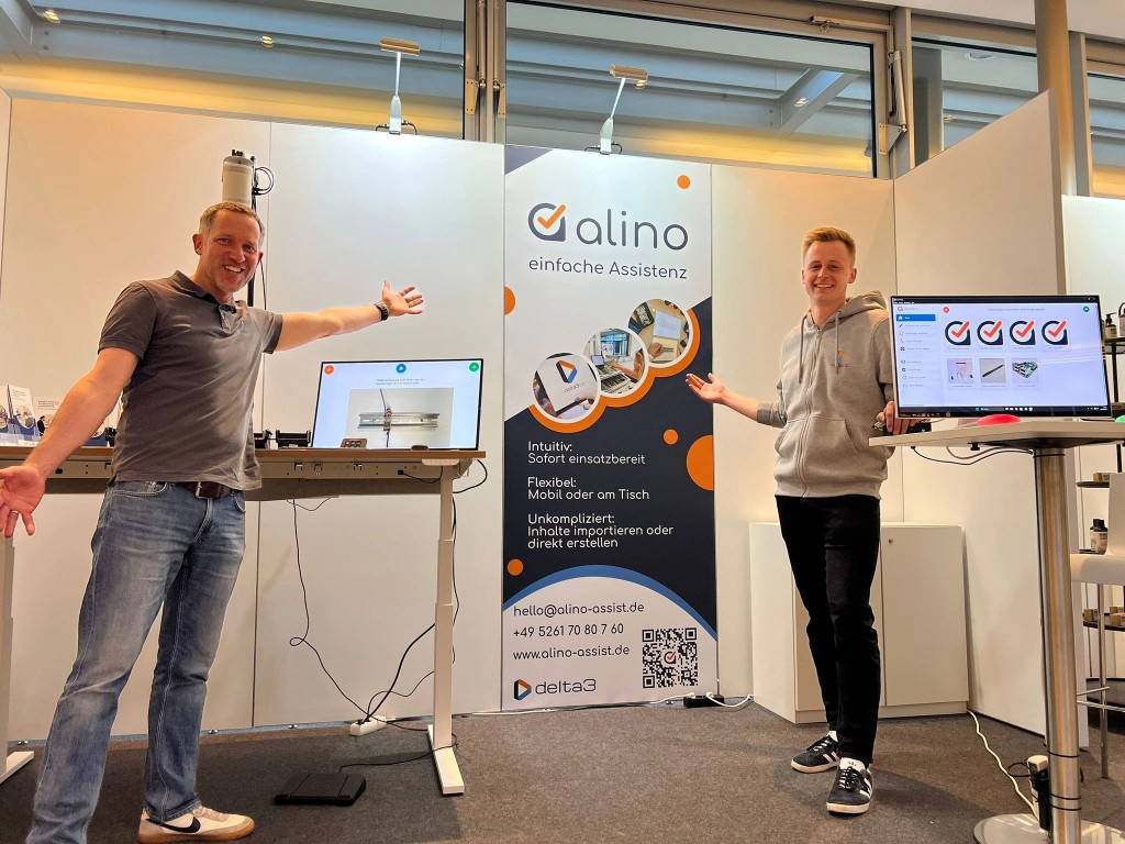 Zwei delta3 Mitarbeitende präsentieren den alino Messestand mit Assistenz-Software und Monitoren